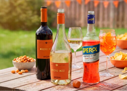3 flessen op een tuintafel met nootjes en chipjes erbij met een glas witte wijn en glas aperol spritz